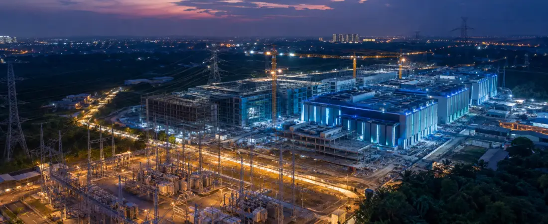 Asia-Pacific data center campus under construction beside high-voltage power infrastructure at dusk