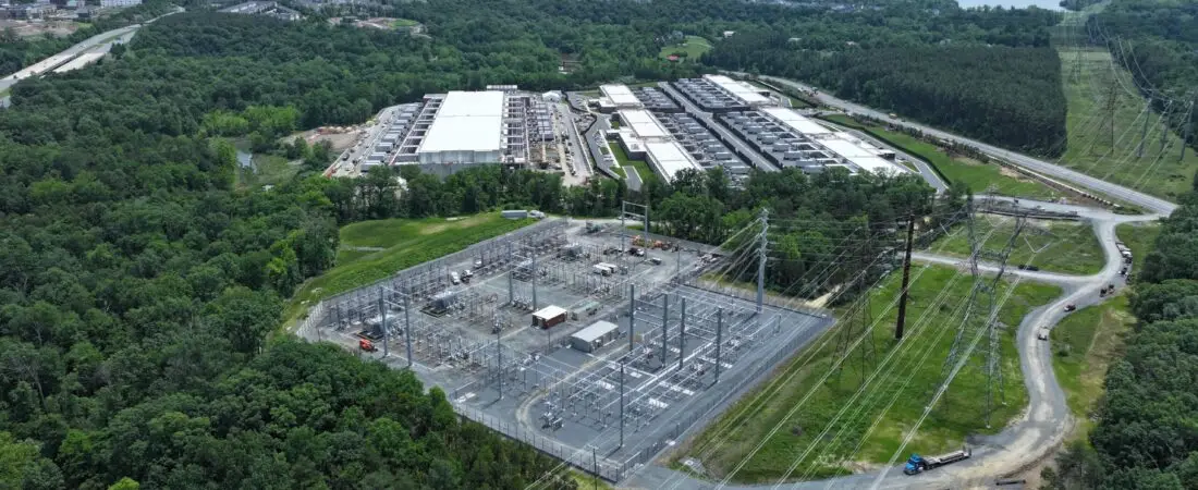 Aerial view of a data center campus beside a high-voltage electrical substation and transmission infrastructure.